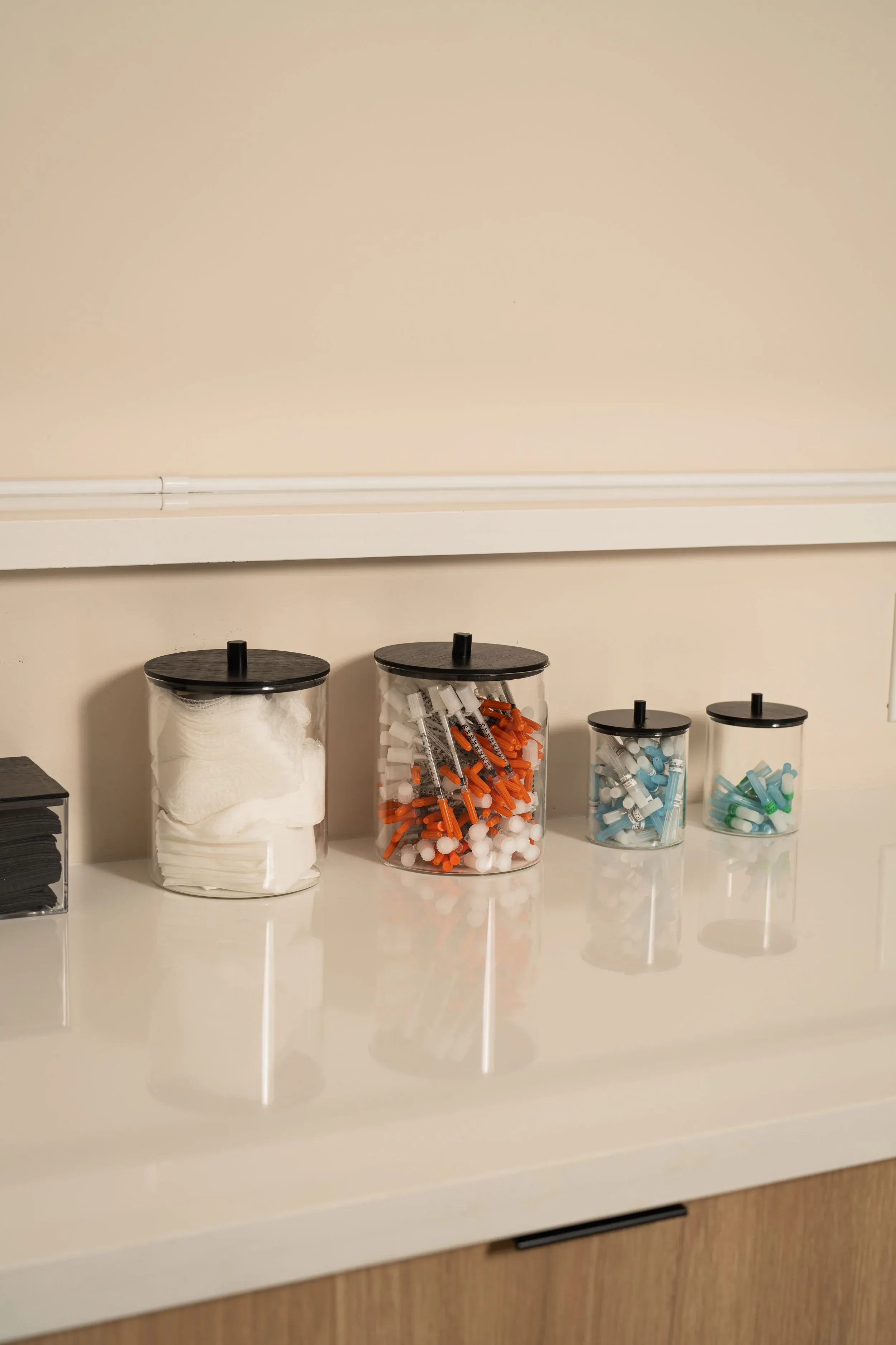 Lidded glass jars of gauze and capped syringes lined up on the white treatment counter